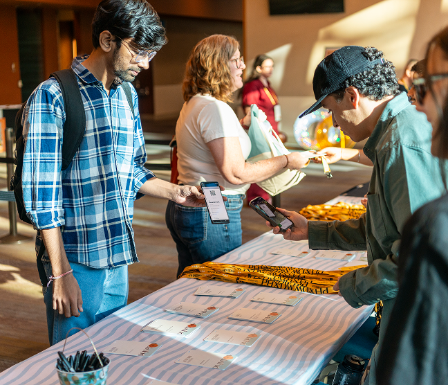 Conference attendees check in at the PHXDW 2024 registration table, scanning QR codes on their phones to pick up name badges and lanyards.