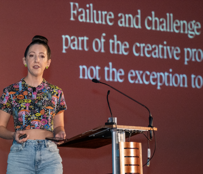 A keynote speaker presents in front of a red screen that reads “Failure and challenge are part of the creative process, not the exception to it” during PHXDW 2024.